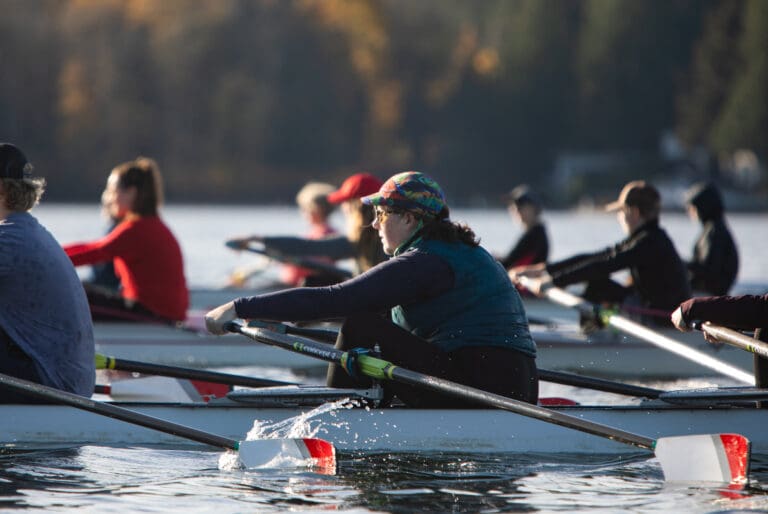 A woman in a boat on the lake rows among teammates.
