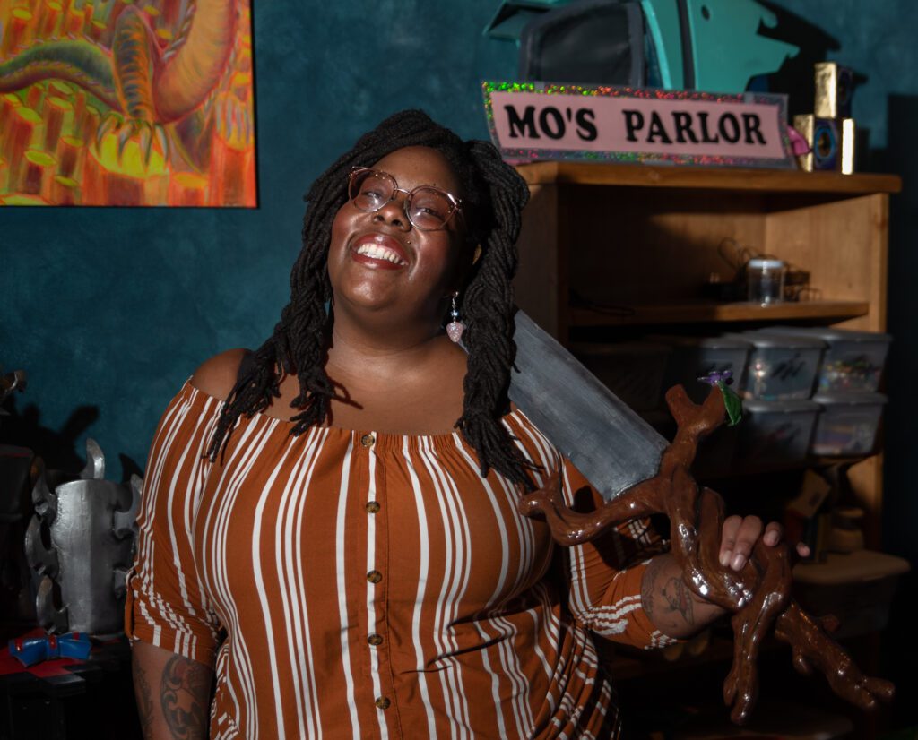 Monique Green holds a sword in front of a pink sign labeled 'Mo's Parlor' in her downtown Bellingham studio.