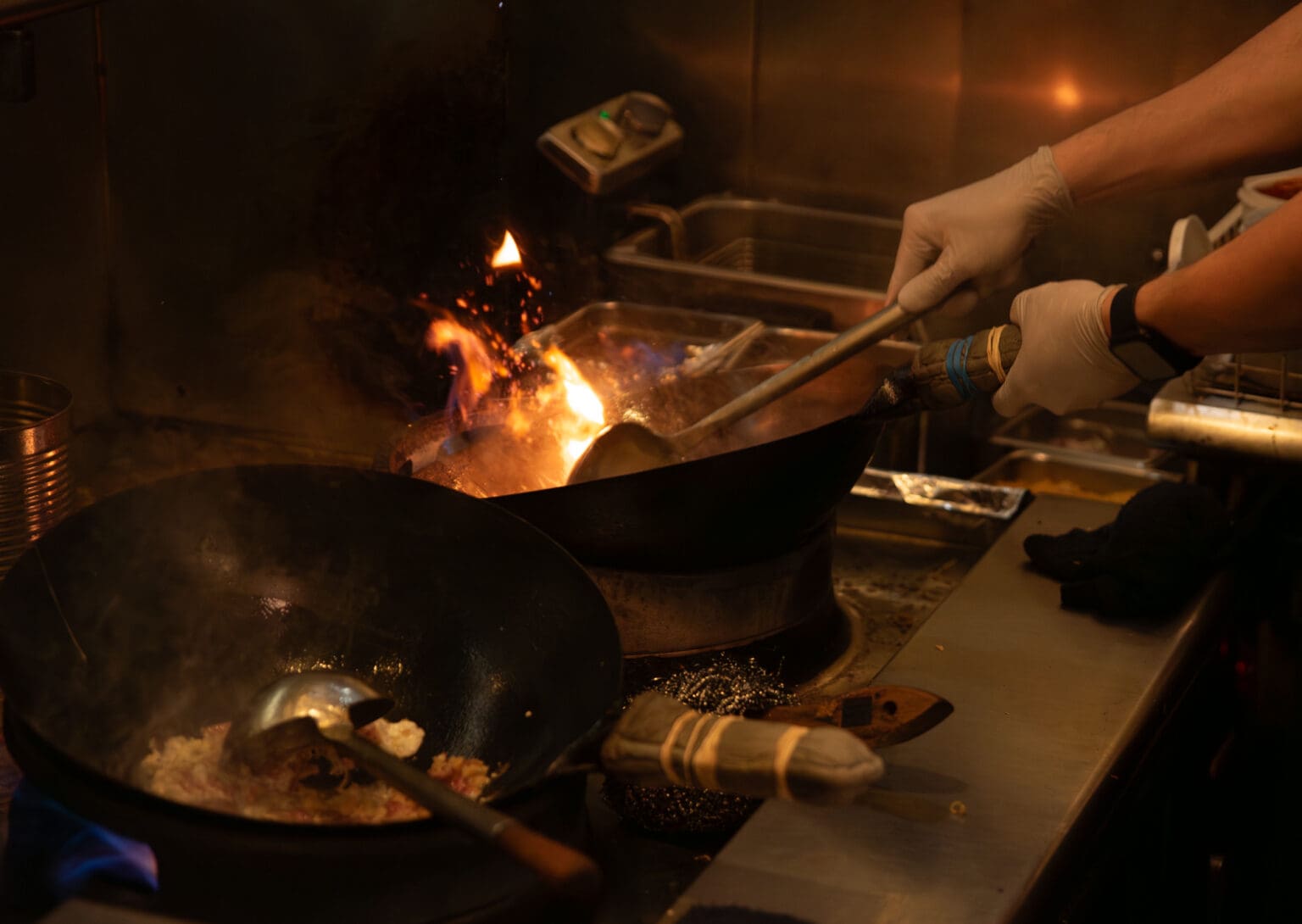 A chef at Rachawadee Thai Cafe fires up a wok as he cooks a meal over the bright heat.
