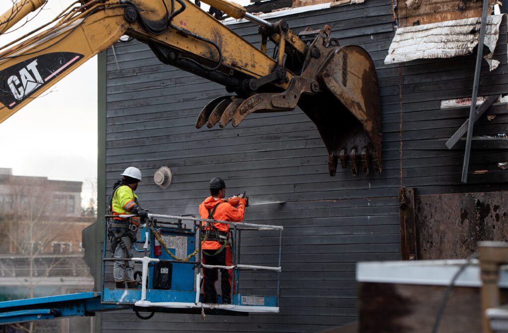 A worker cuts through the siding of the Terminal Building as the wall is propped up by an excavator.