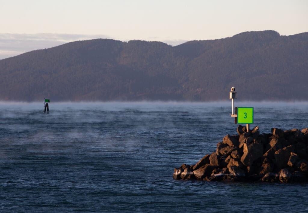Steam rises off of Bellingham Bay as a bright neon sign is planted in the rocks displaying the number 3.