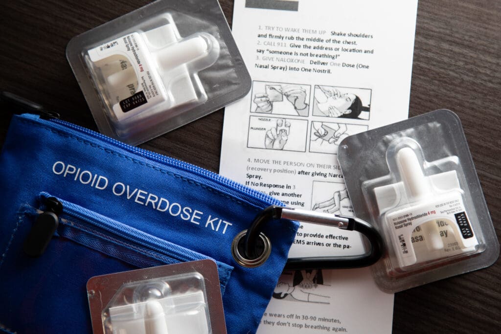 Naloxone next to an opioid overdose kit set on the table as instructions on how to help are laid out.