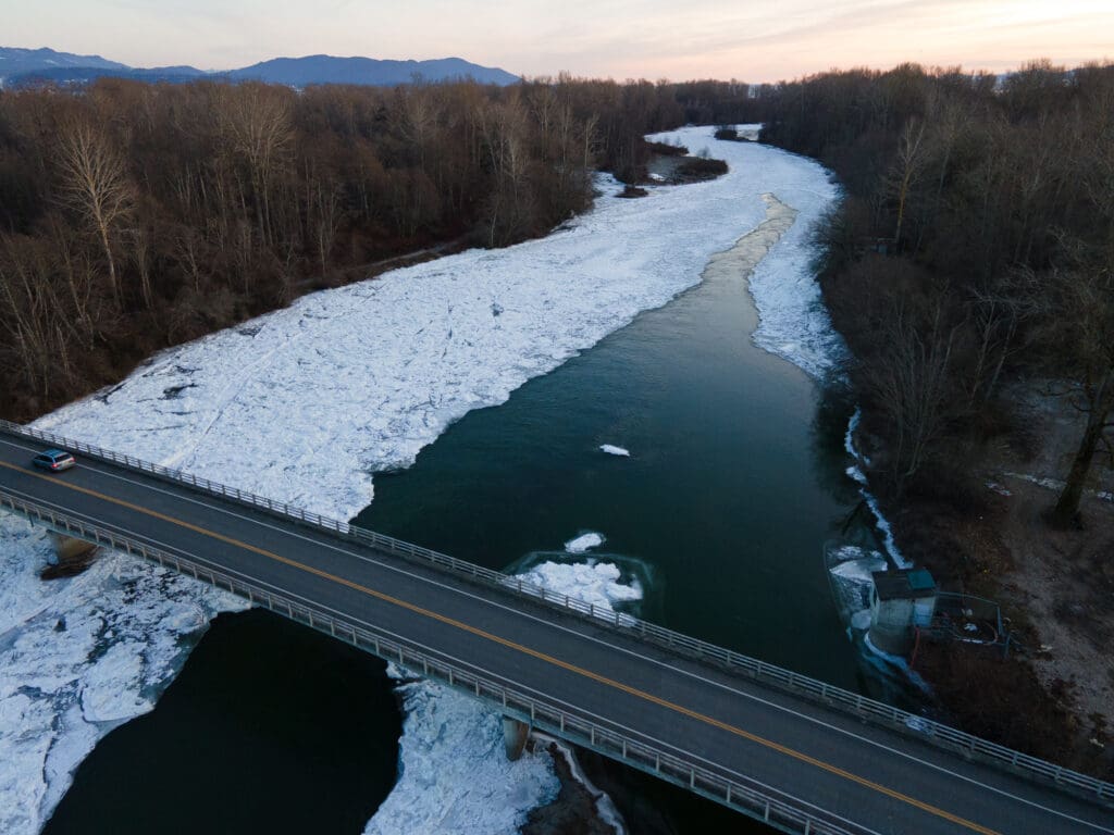 The Nooksack River, covered in sheets of ice and snow, snakes toward Bellingham Bay beneath the Marine Drive bridge.