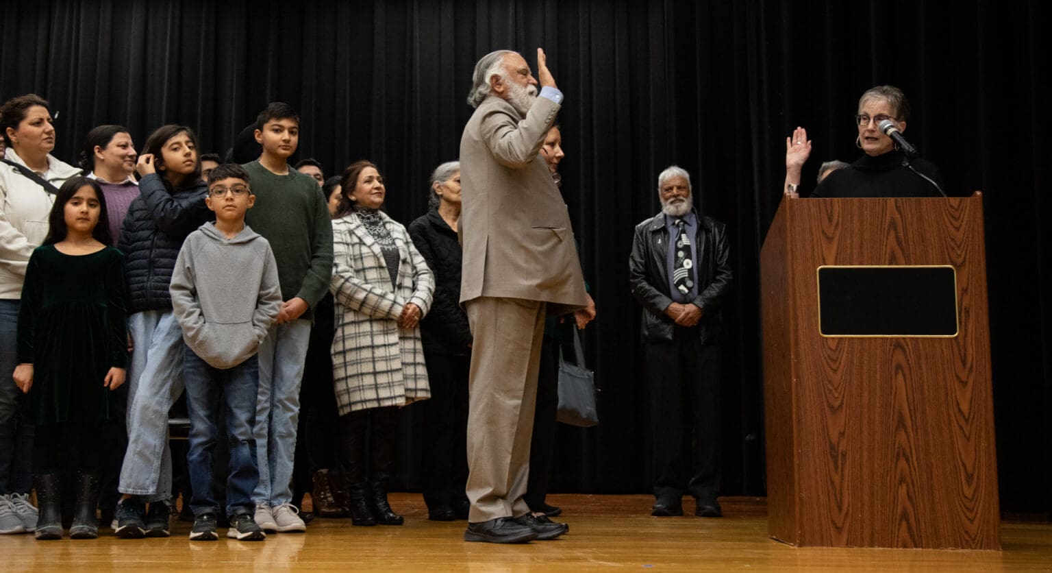 Surrounded by family, Satpal Sidhu is sworn in by county Auditor Diana Bradrick behind a wooden podium.