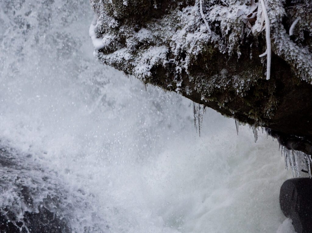 Icicles cling to rocks next to Whatcom Falls with white powdery snow on rocks and moss..