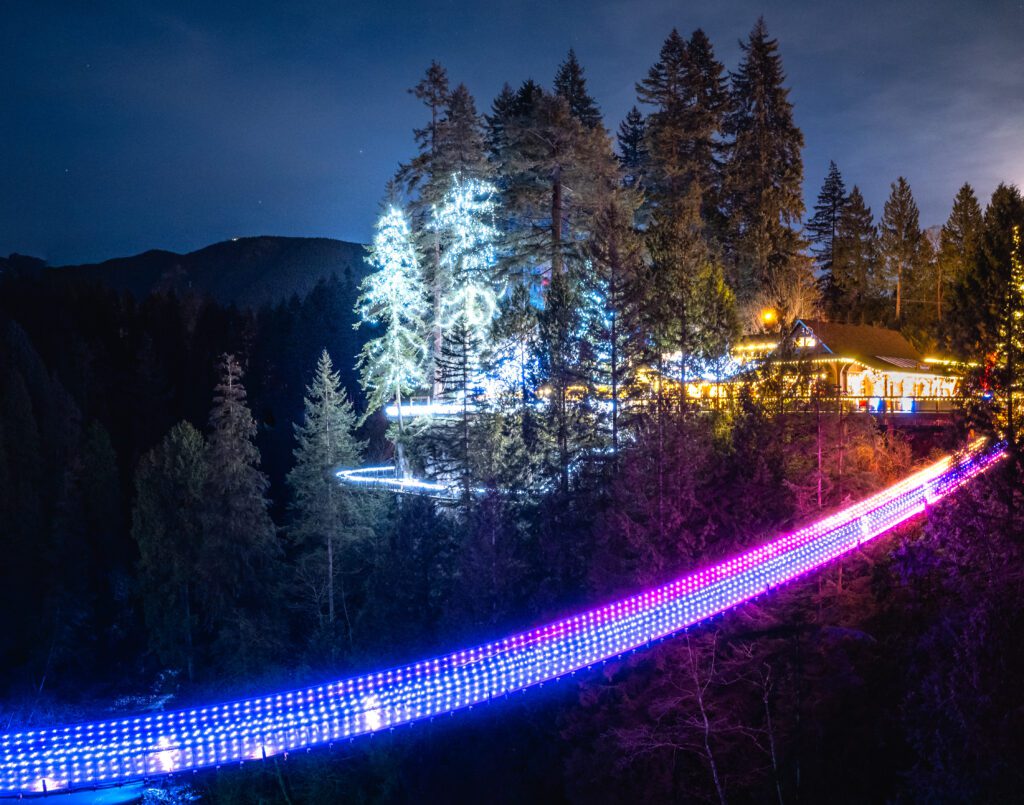 A bridge is lit up by brightly colored lights that lead to the cabin that is also lit up by the same type of lights but in different colors.