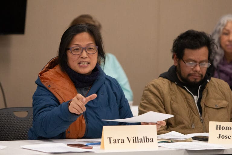 Immigration Advisory Board member Tara Villalba invites audience members to share their thoughts as she gestures with her hand as she speaks next to other board members.