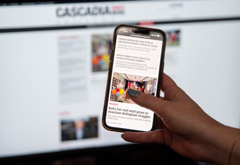 A person holding up a phone showing a page on Cascadia Daily News' new website.