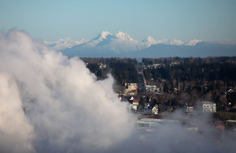 Snow-covered Canadian mountains are visible beyond downtown Bellingham as clouds cover most of the town.
