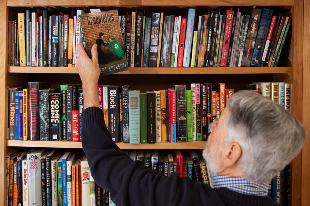 Rob Lopresti pulls down one of the books he wrote — "Greenfellas" from the top shelf filled with books.