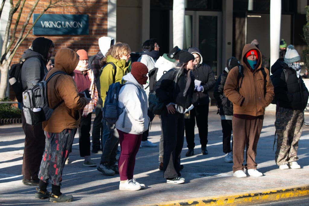 Crowds of Western Washington University students dressed in heavy winter clothes as they patiently wait at the bus stop.