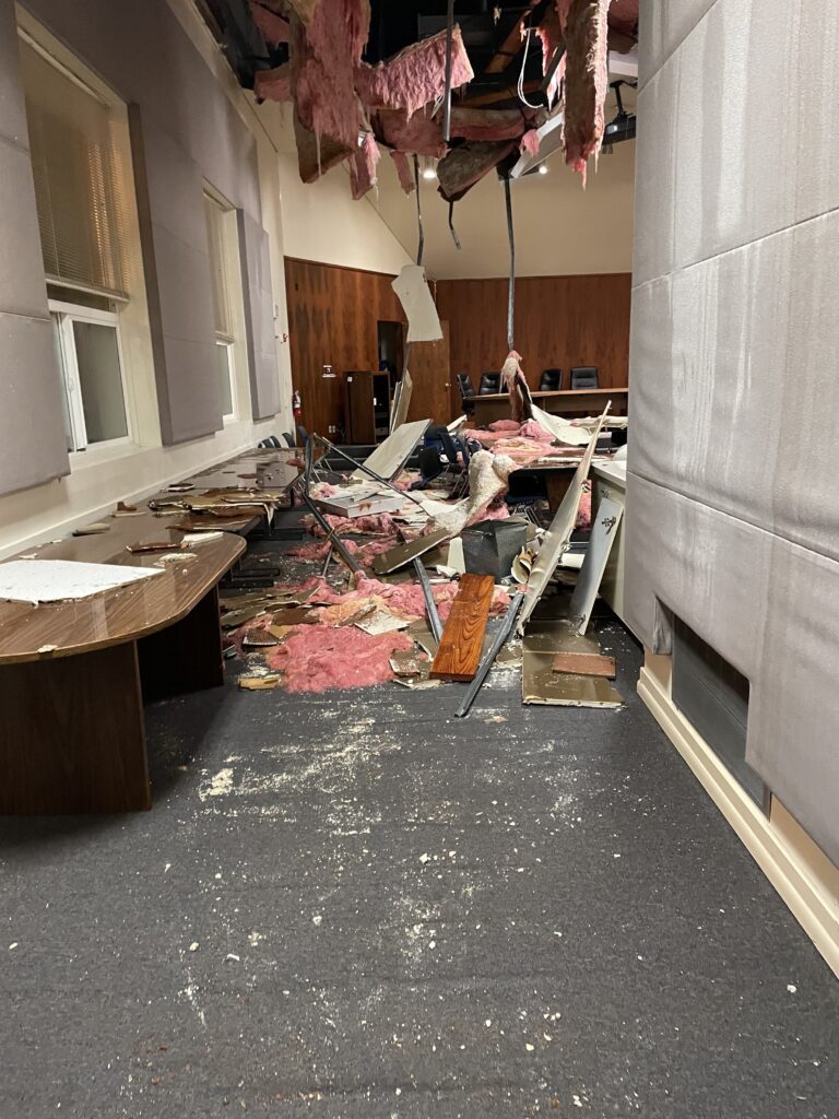 An opening in the ceiling has dropped debris and pink insulation into the room.