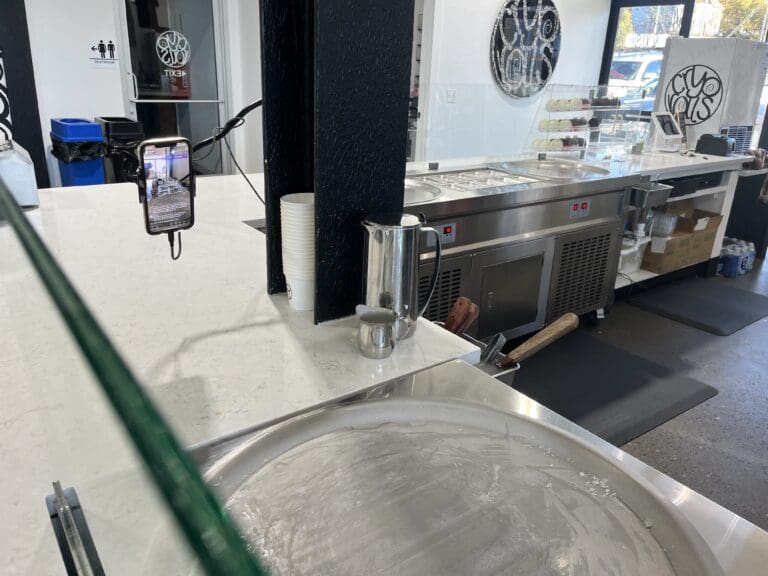 An iPhone propped to livestreams to TikTok the icy surface where employees roll ice cream.