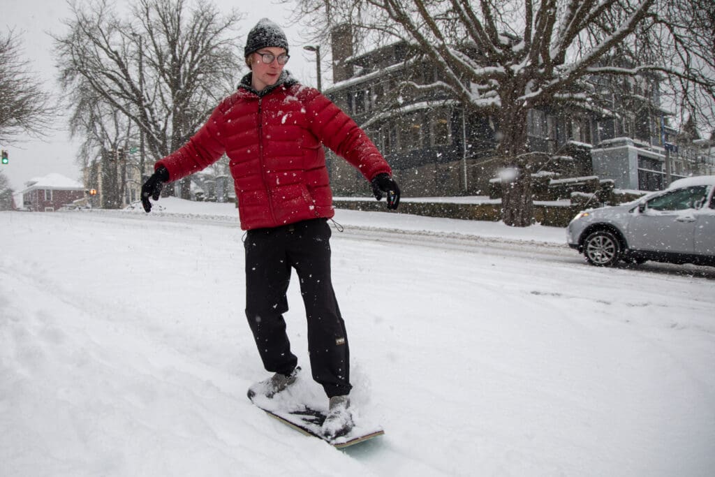 Will Lord, 22, rides a snow skate down Chestnut Street wearing a bright red winter vest.