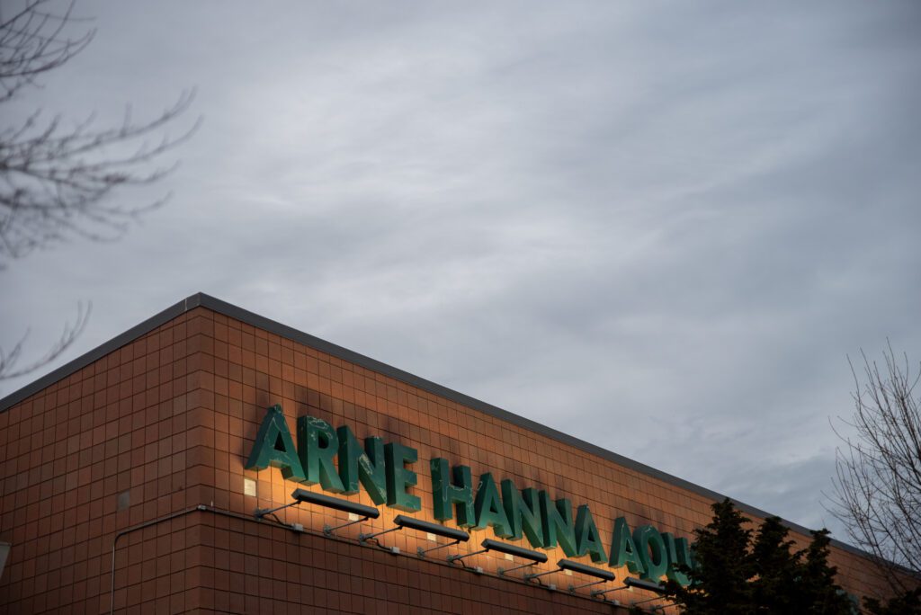 The Arne Hanna Aquatic Center signage lit up by lights as clouds cover up the sky above.