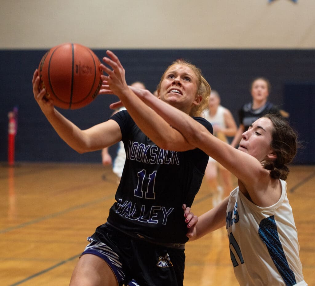 Nooksack Valley junior guard Kate Shintaffer leaps to try and take a shot as a defender reaches over her for the ball.