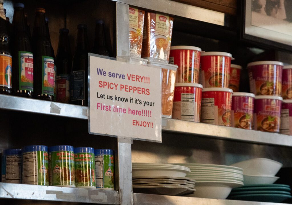 Rachawadee Thai Cafe's shelf stocked full of spices, curries and plates has a sign warning customers of the spice levels.