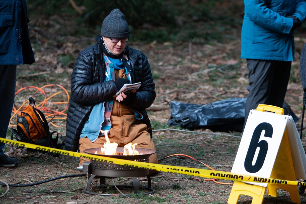 Jesse Nussbaum of Cascade Cross curls up by a fire with a book and pen behind the yellow caution tape.