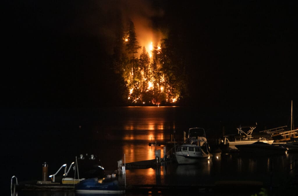 A wildfire burns late into the night with the flames reflecting into the dark water.