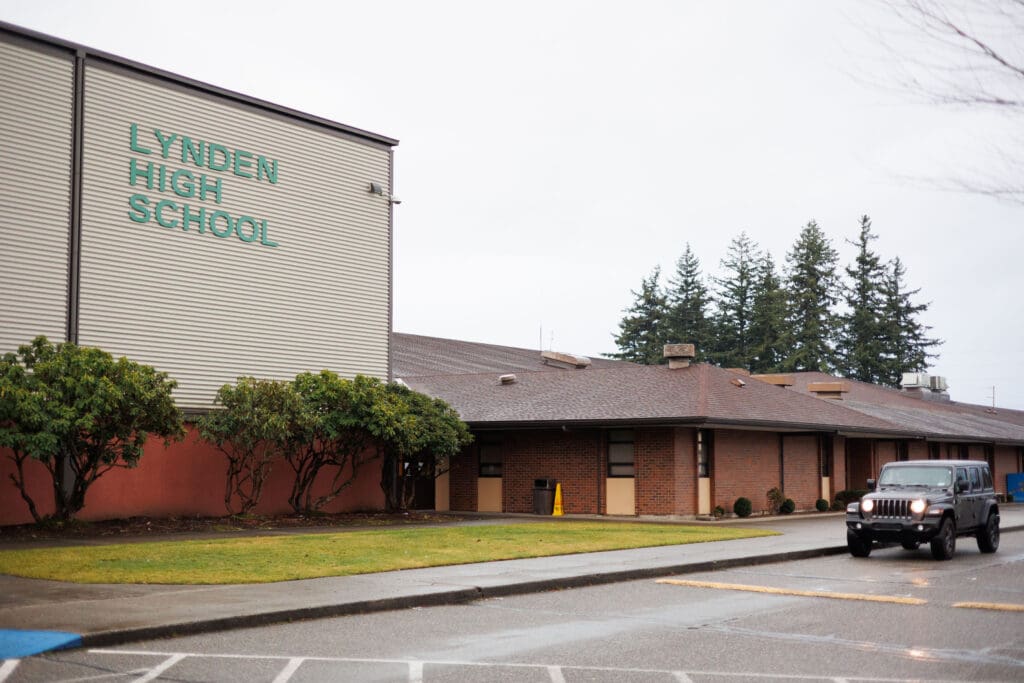 Lynden High School is bright blue lettering as a car is parked next to the school buildings.