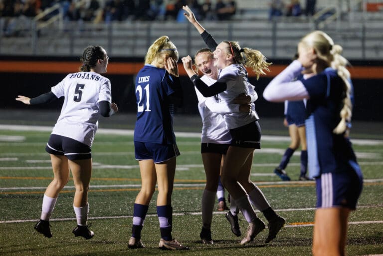Meridian’s Morgan Adams raises her hands in celebration after scoring a goal as her teammates rush to celebrate with her.