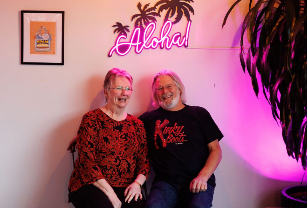 Before getting into costume at Mrs. Claus and Santa Claus, Lynn and Doug Starcher pose at Culture Cafe underneath an "Aloha!" neon sign.