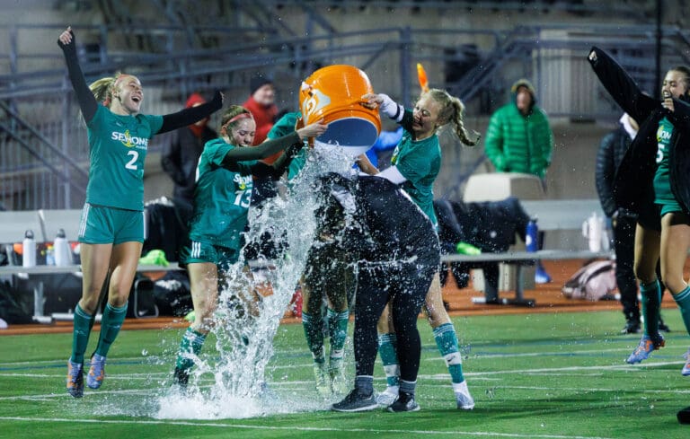 Sehome players dowse head coach Emily Webster with water from their orange water cooler as others watch and celebrate.