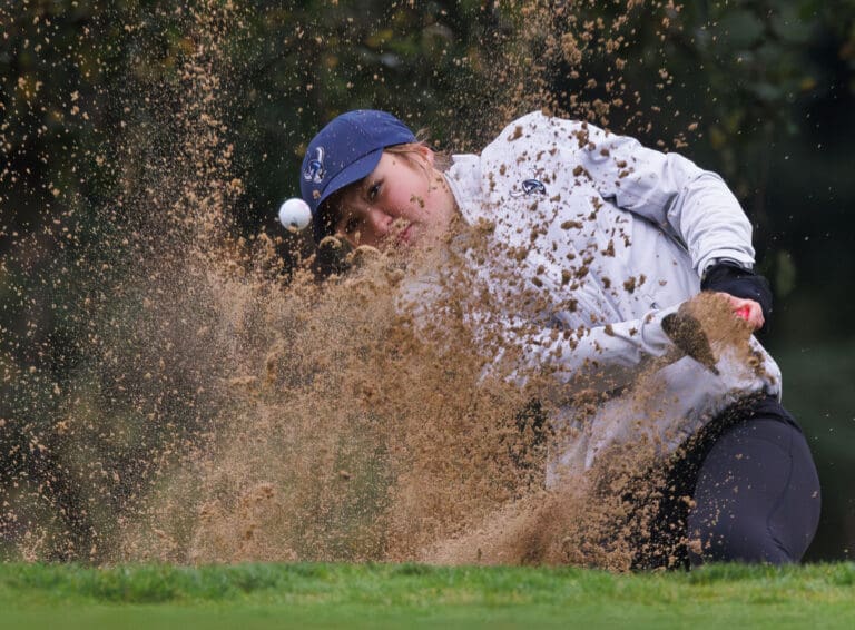 Western Washington women's golfer Emma Worgum hits out of a bunker as dirt fly out.