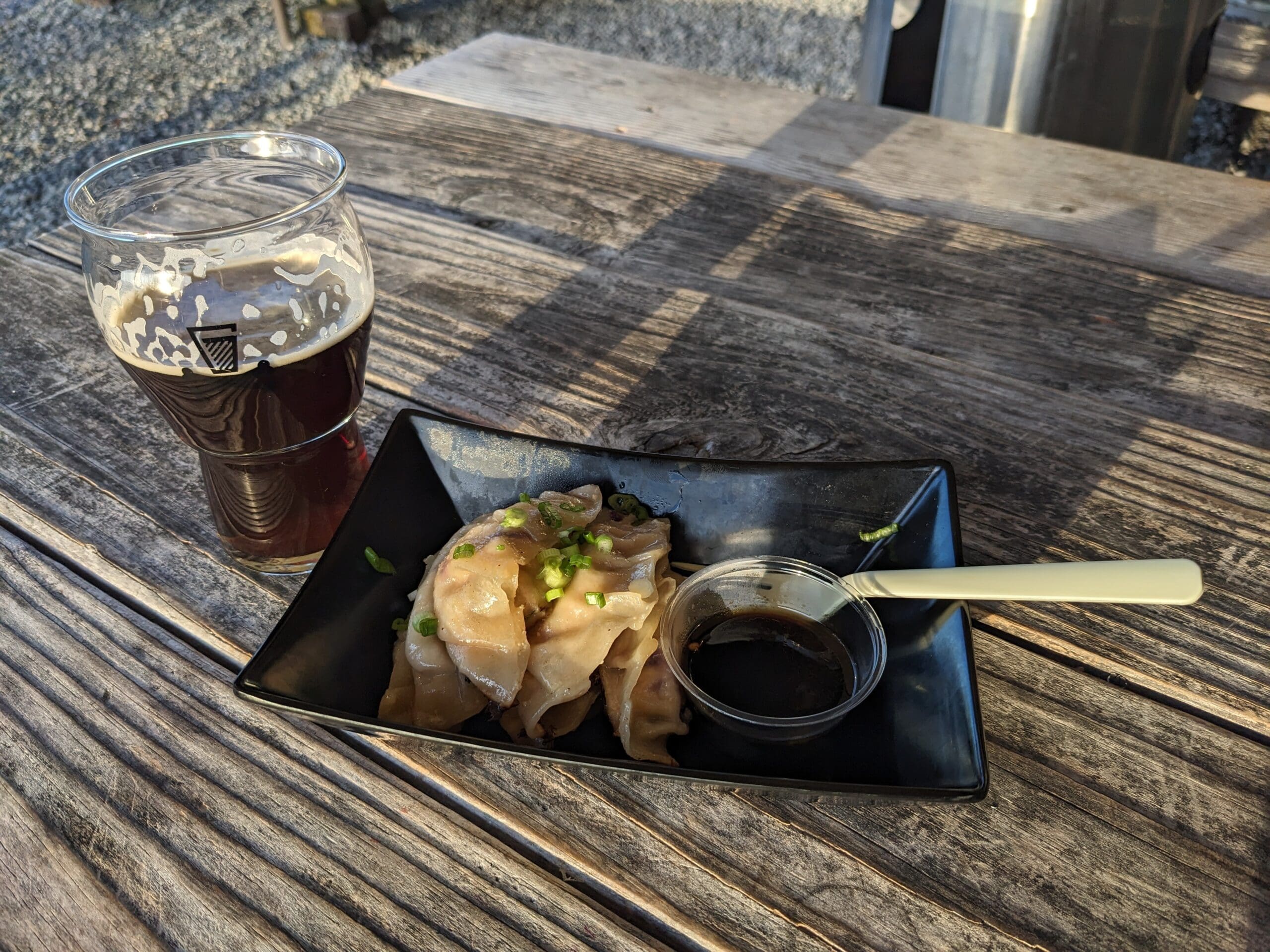 House-made tofu gyoza with a side of sauce and chopsticks, and a dark ale placed on a wooden table.