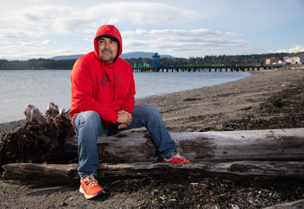A man in a red hoodie sitting on a log on the beach.
