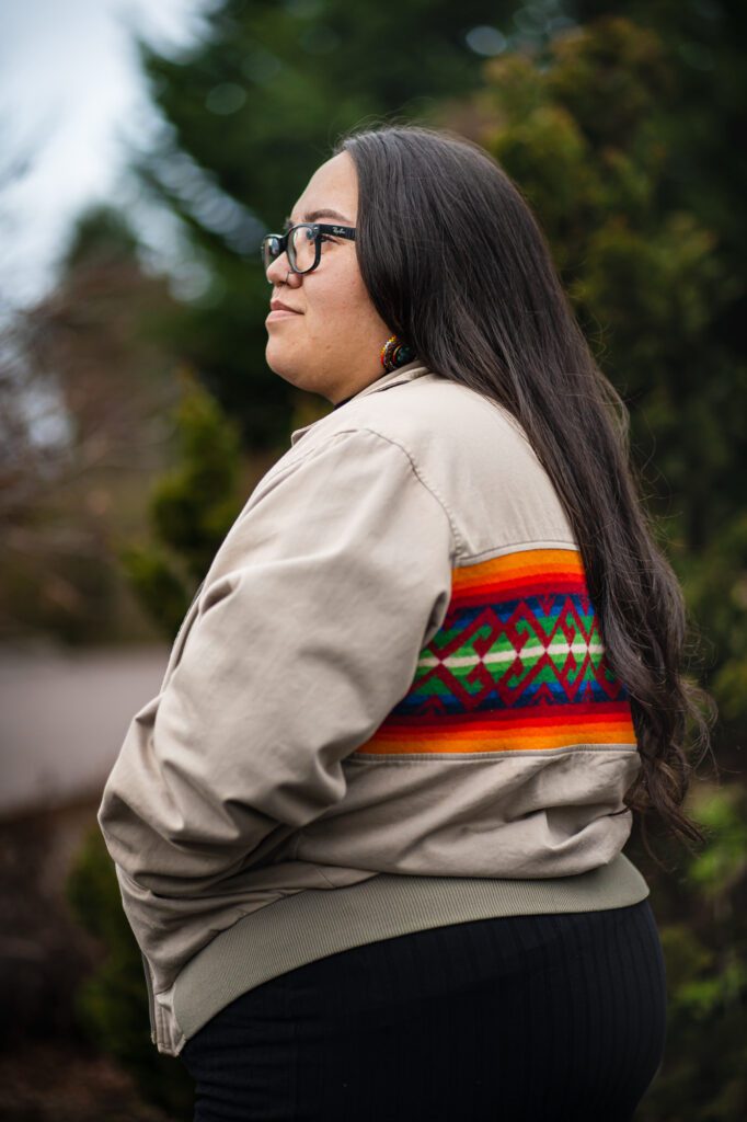 A side profile of Noelani Auguston with her hands tucked in her multicolored jacket.