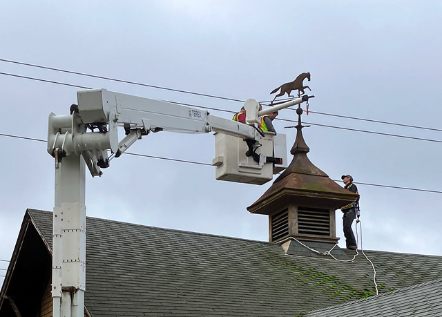 Staff from Bellingham parks remove the weather vane from a parks department building at the end of a white crane.