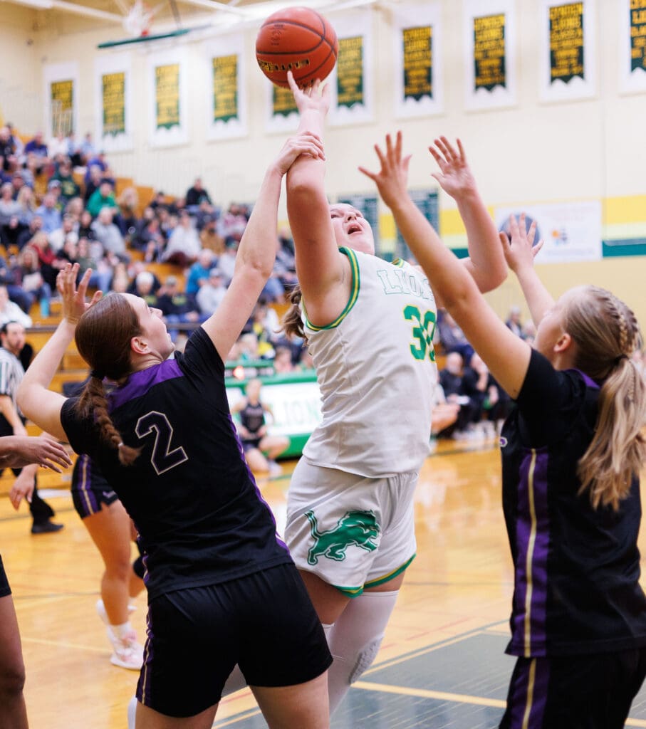 Lynden’s Payton Mills leaps into the air in an attempt to shoot a basket as two defenders reach with their hands as they tried to block the shot.