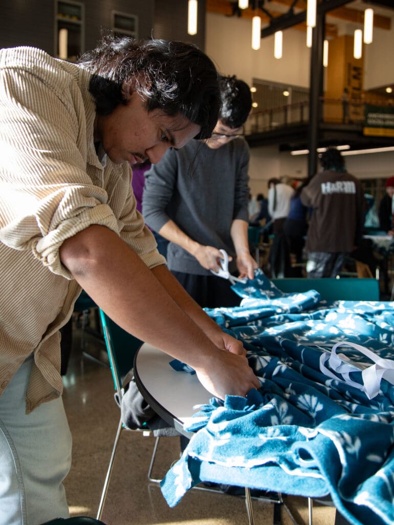 Danny Brown, left, and Sam Kim from Western Washington University cut and tie two sheets of fleece into one thick blanket.