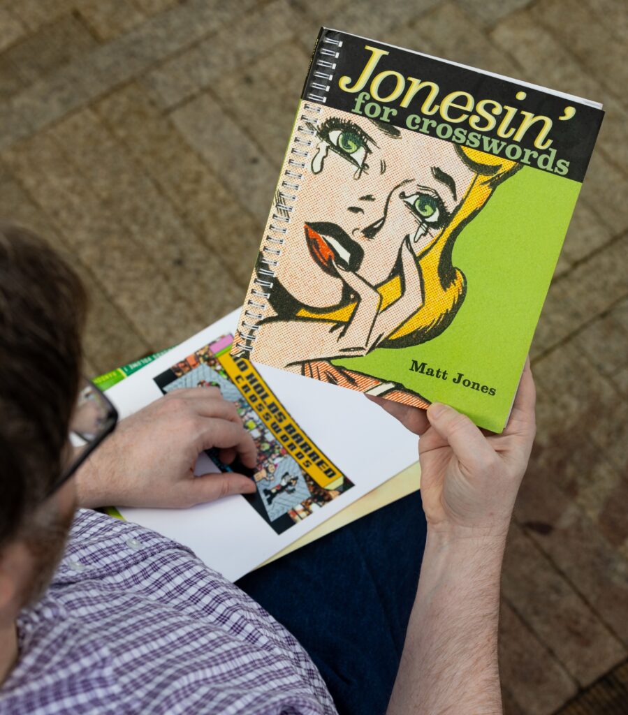 A person holds up a copy of "Jonesin' for crosswords".