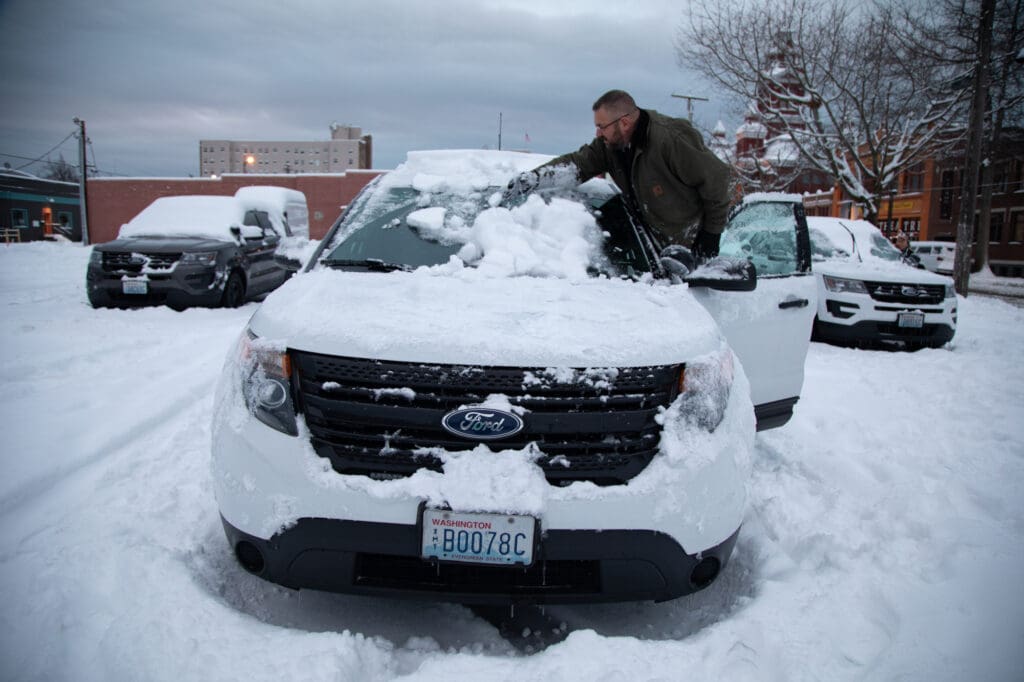 Jason Karb wipes snow off a Whatcom County Sheriff's vehicle in the parking lot next to the courthouse.