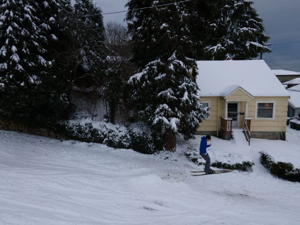 A skier takes a jump down Chestnut Street past the trees and the yellow house.
