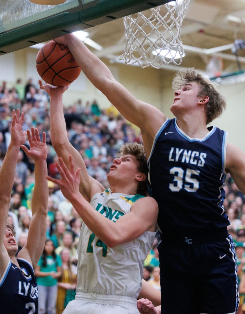 Lynden Christian's Jeremiah Wright leaps to block a shot by Lynden's Kobe Baar as another player tries to help.