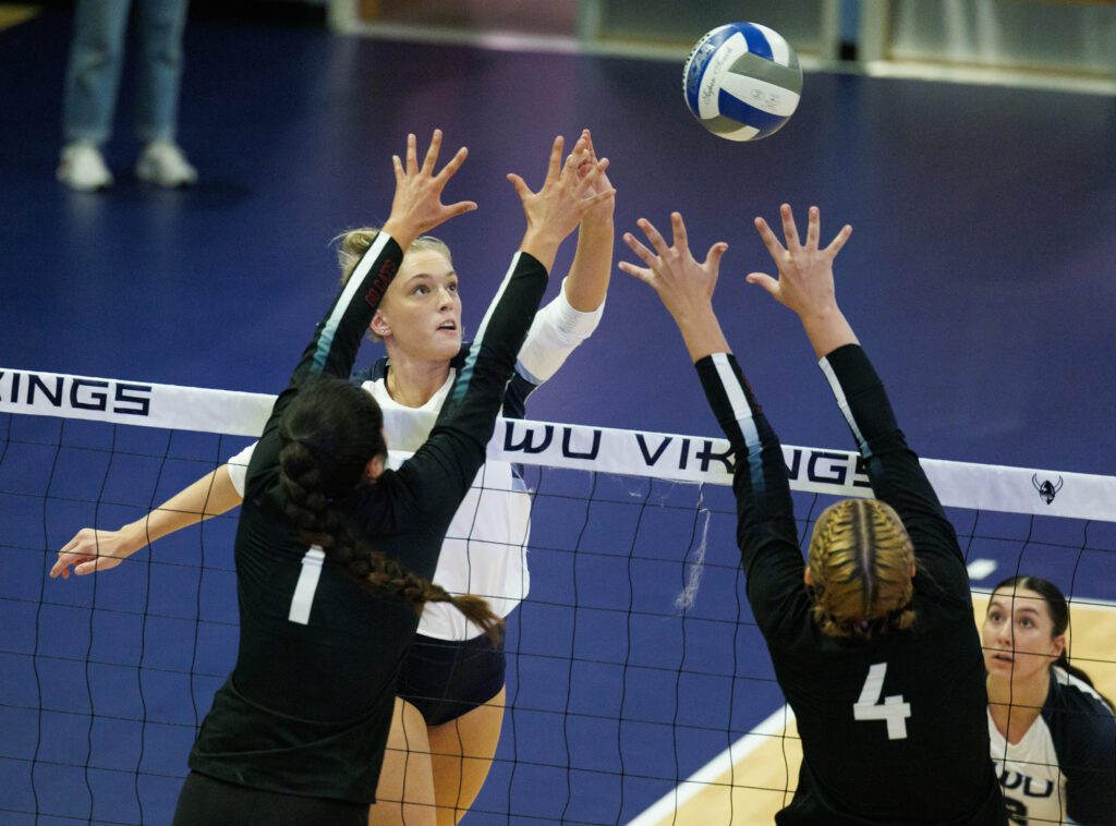 Western Washington University's Gabby Kepley taps the ball over Wildcats defenders as her spiker watches from the side.