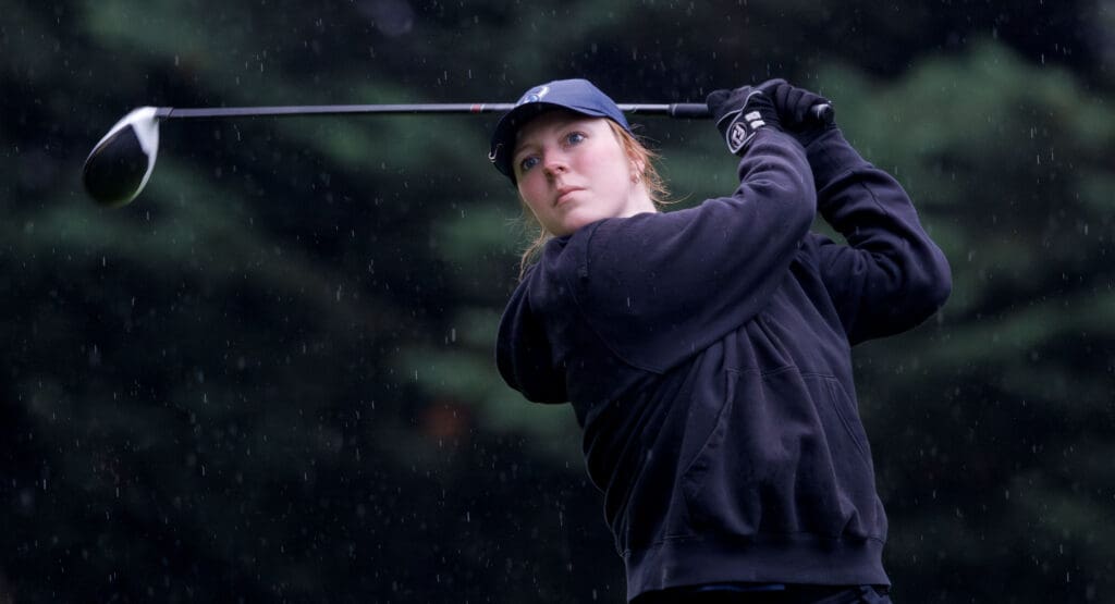 Western Washington's Dani Bailey after a swing, the golf club behind her as snow falls around her.