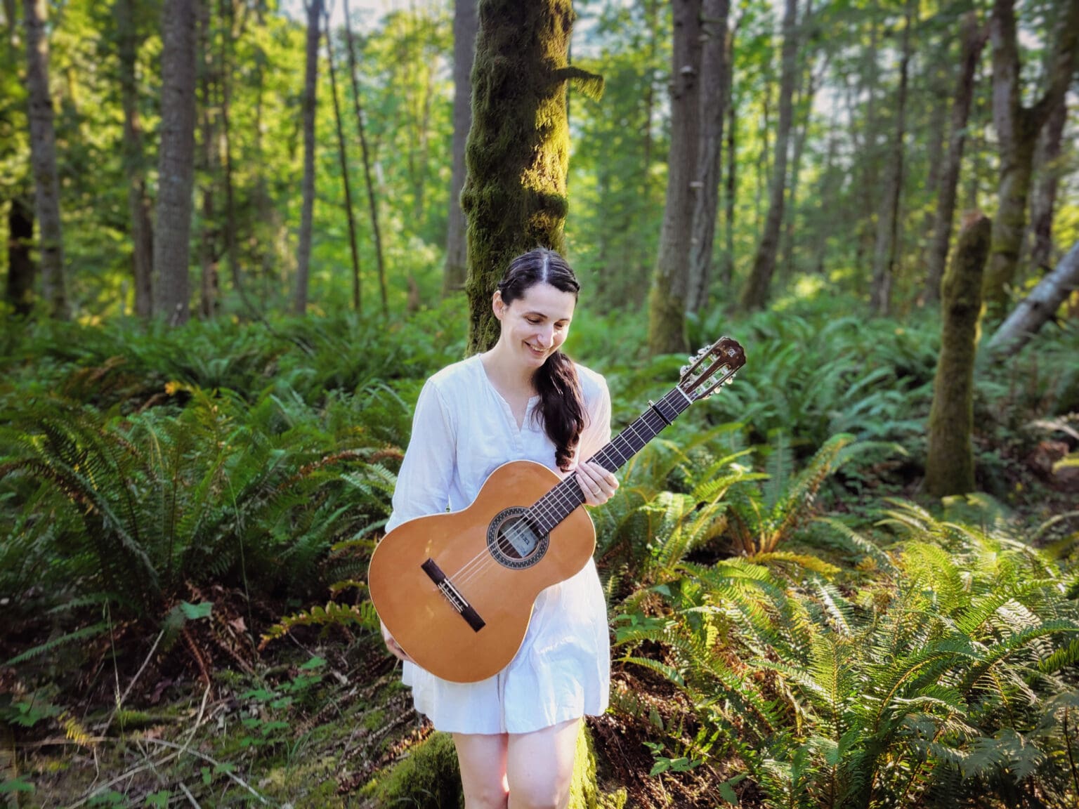 Singer-songwriter Octavia McAloon holding her acoustic guitar in the middle of a lush forest.