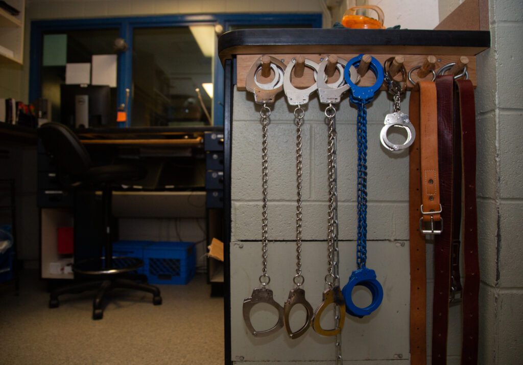 Different colors and sizes of handcuffs and belts hang from a rack in the booking office of the Whatcom County Jail.
