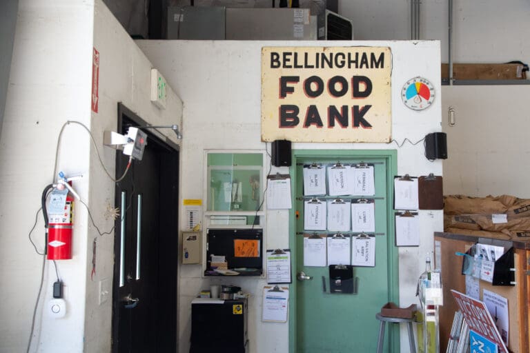 The Bellingham food bank sign hangs over a green door with papers taped to it.