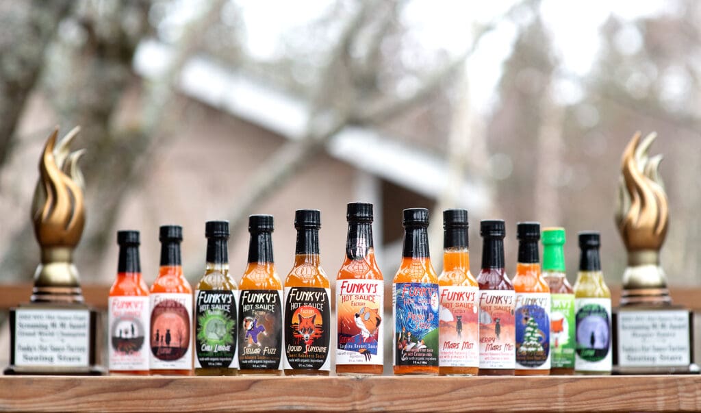 Local business Funky's Hot Sauce Factory different flavors lined up on a wooden table side by side inbetween two awards.