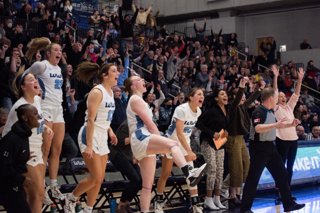 Western Washington University women's basketball erupts in cheers as they all jump and stand from their seats as the crowd cheer along with them.