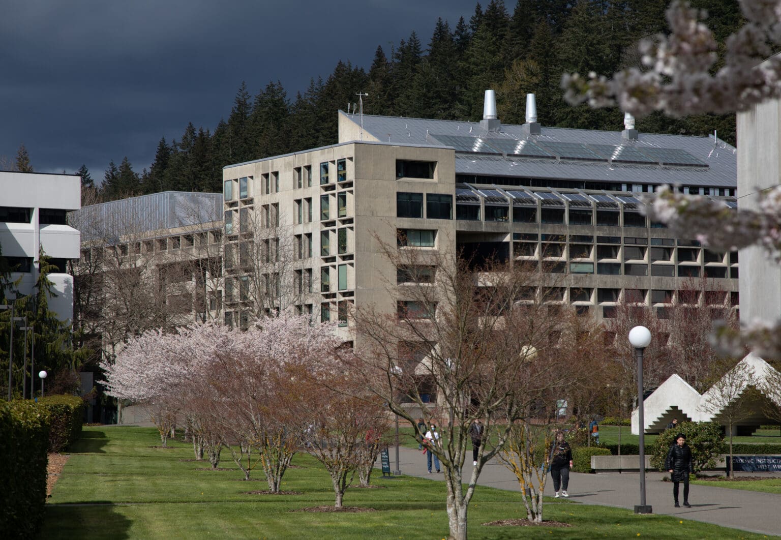 Western Washington University parking building behind trees as students walk to their classes.