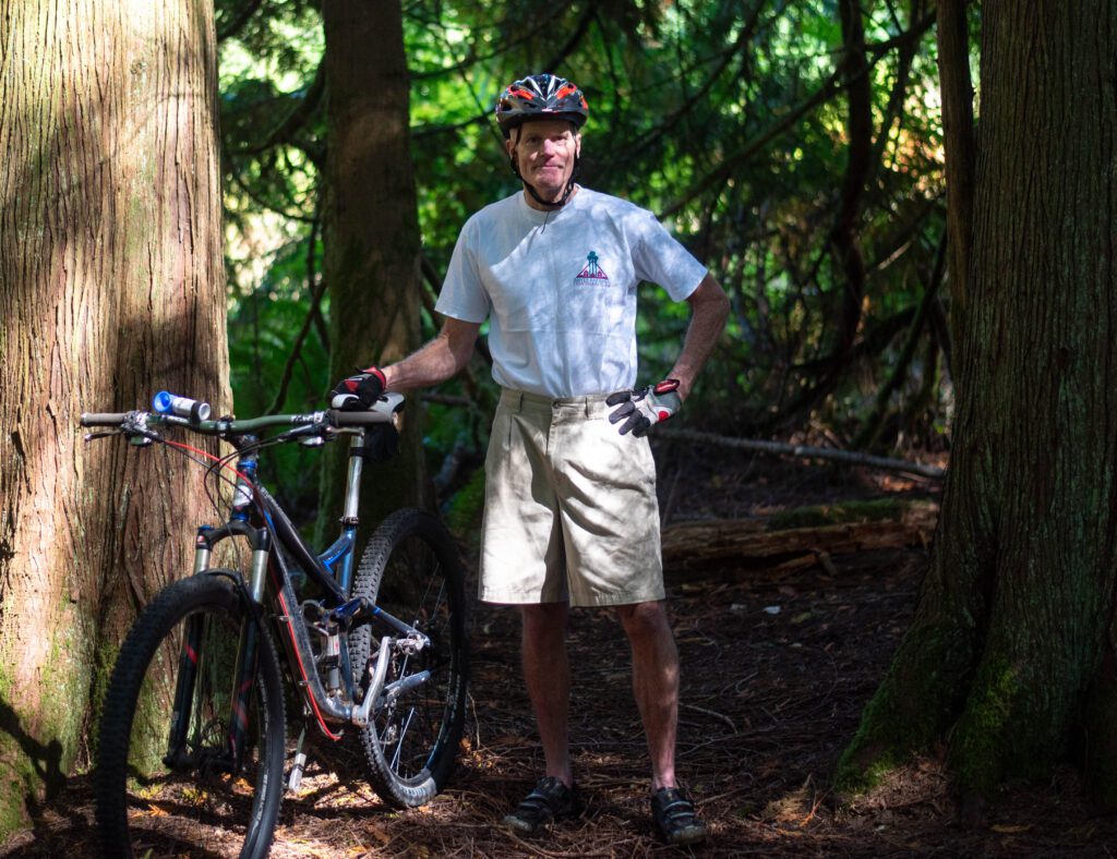 Bellingham mountain biker Mike Lanham stands in between trees as he stands next to the bike.
