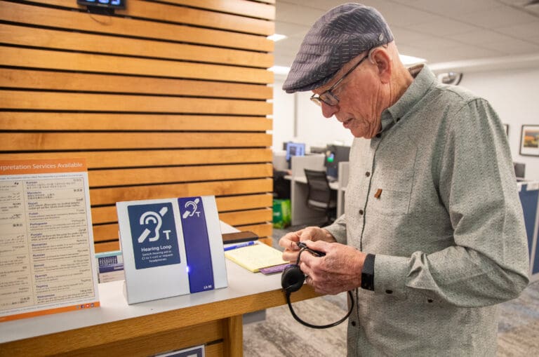 Larry Wonnacott fiddles with headphones at a hearing loop station in the Bellingham Public Library as a small sign on the table informs the visitor on the proper usage.