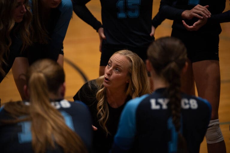 Lynden Christian volleyball head coach Kristy Van Egdom talks to her team as she is surrounded by her players in a small crowded huddle.
