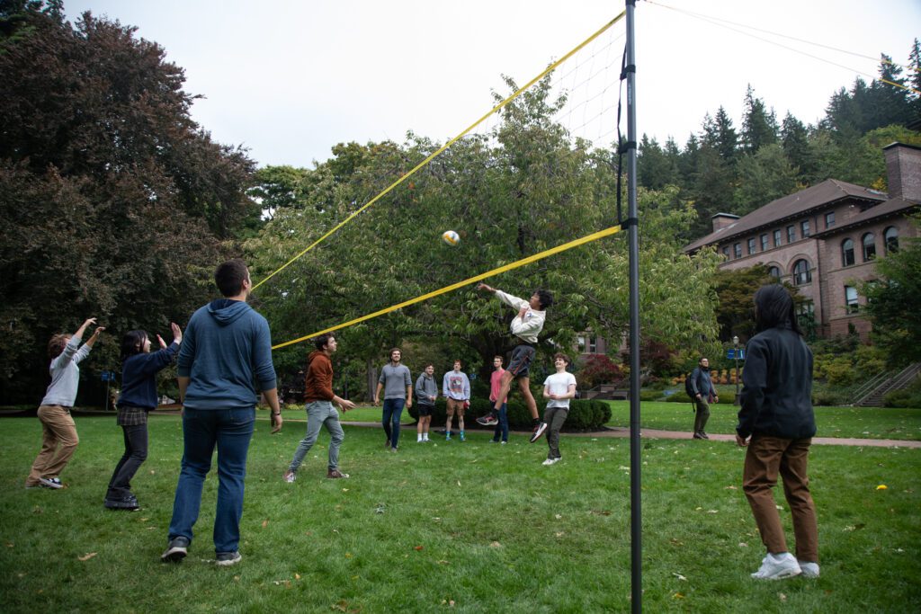 Students play volleyball on the lawn of Old Main as a player leaps into the air to hit the ball over the net.
